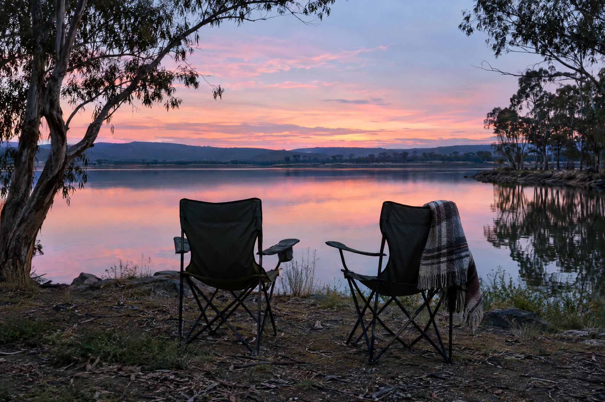 Two camp chairs facing a still lake at dusk
